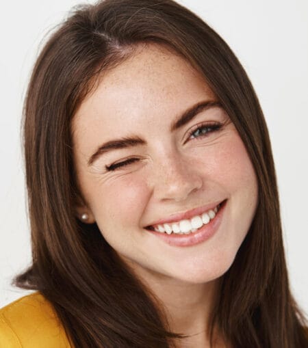 Close-up of cute and dreamy young woman smiling, winking at camera to encourage client, standing over white background